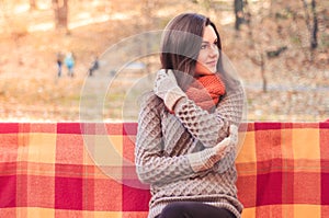 Young beautiful woman in a knitted sweater sitting on a bench in an autumn park