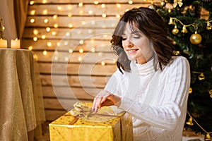 Young beautiful woman in knitted white dress sits on floor near christmas tree