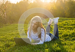 Young beautiful woman with a laptop lies on the grass in sunset
