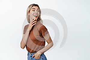 Young beautiful woman laughing, smiling and looking behind her shoulder at empty space, logo or advertisement text