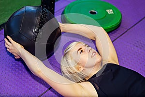Young beautiful woman laying on back during exercise with med ball at gym or fitness club. Abdominals or back mucles workout