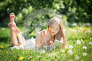 Young beautiful woman lies on a grass and reads the book