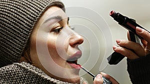 Young beautiful woman with lipstick brush is standing and looking at mirror