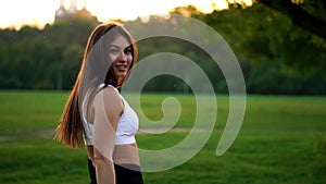 Young beautiful woman listening music at park while running. Portrait of smiling sporty girl with earphone looking at