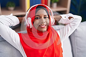 Young beautiful woman listening to music sitting on sofa at home