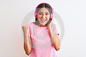 Young beautiful woman listening to music using headphones over isolated white background screaming proud and celebrating victory