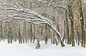 Young beautiful woman with little daughter having fun in snowy forest. Pleasant family time in winter