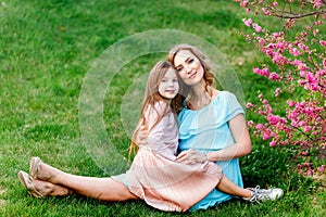 Young beautiful woman with a little daughter walking through the blooming sakura.The concept of family rest and love