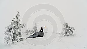 Young beautiful woman in long black dress with old lantern over winter hill background and snowfall. Fairy tale girl on polar