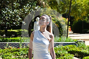 Young and beautiful woman with long blond hair and a short white dress is in a famous park in seville rich in vegetation, spain.