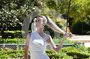 Young and beautiful woman with long blond hair and a short white dress is in a famous park in seville rich in vegetation, spain.