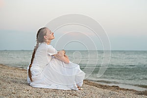 Young beautiful woman with long braid sits by the sea and dreams