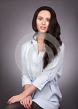 Young beautiful woman with long dark hair and blue shirt posing on gray