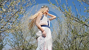 Young beautiful woman in long dress standing in spring blossom garden