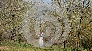 Young beautiful woman in long dress standing in spring blossom garden