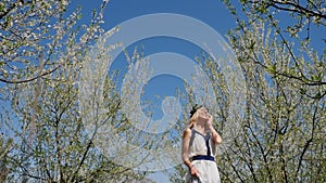 Young beautiful woman in long dress standing in spring blossom garden