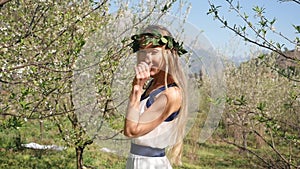 Young beautiful woman in long dress walking in spring blossom garden