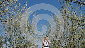 Young beautiful woman in long dress walking in spring blossom garden