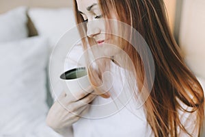 Young beautiful woman with cup of coffee or cacao in bed at home. Girl having breakfast in bed. Morning concept