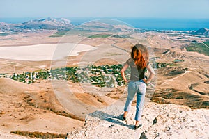 A young beautiful woman with long hair and jeans sits in joga pose on a rock in the Koktebel valley in Crimea. The landscape of sa