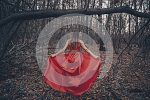 Young beautiful woman in the long red dress is walking along foggy mysterious forest