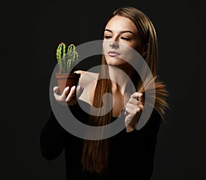 Young beautiful woman with long silky straight hair in black body holding cactus plant in pot and comparing with split