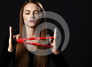 Young beautiful woman with long silky straight hair in black clothes with eyes closed holding red hair straightener