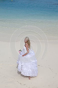 Young beautiful woman in a long white bride dress on the sand on the beach by the blue sea