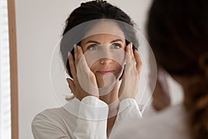 Young beautiful woman look in mirror massaging face