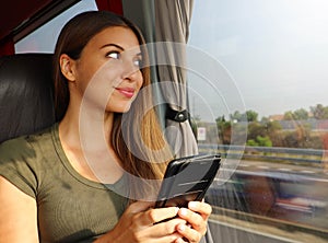 Young beautiful woman looking through the bus window. Happy bus passenger traveling sitting in a seat and looking through the