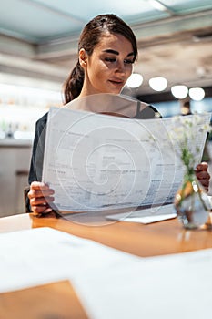 Young beautiful woman looking at menu deciding what to order in modern cafe.