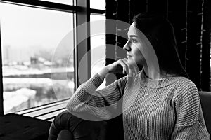 Young woman looking out the window while sitting in a chair on a winter day