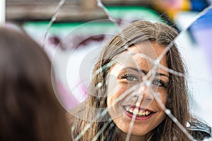 A young, beautiful woman looks at her reflection in a broken mirror