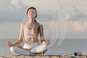 Young beautiful woman in lotus position meditation on beach. Woman practicing yoga in sea background