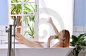 Young beautiful woman lying in bathtub and taking bath near open bathroom window