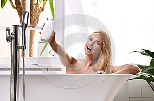 Woman lying in bathtub taking bath near open bathroom window and wash hand with soft shower gel cream lotion