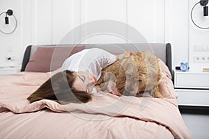Young and beautiful woman lying in the bed and hugging her adorable pet dog