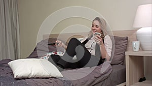 Young, beautiful woman lying on the bed, watching TV and using smartphone