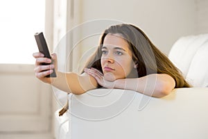 Young beautiful woman lying on couch holding remote control zapping while watching television