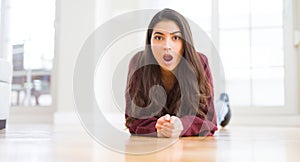 Young beautiful woman lying on the floor at home scared in shock with a surprise face, afraid and excited with fear expression