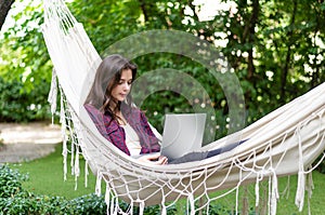 Young beautiful woman lying in a hammock with laptop in a garden. green background. Trees. telework. remote work