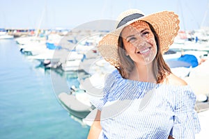 Young beautiful woman at marine port around boats, smiling happy with seaport at the background