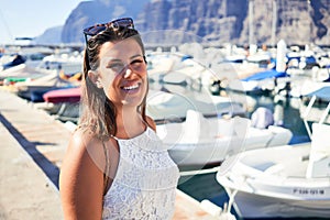 Young beautiful woman at marine port around boats, smiling happy with seaport at the background