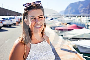 Young beautiful woman at marine port around boats, smiling happy with seaport at the background