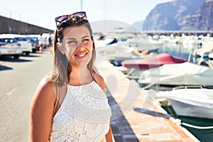 Young beautiful woman at marine port around boats, smiling happy with seaport at the background