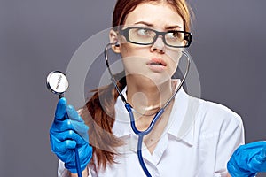 Young beautiful woman in medical gown holds a stethoscope on a gray background, doctor, medicine