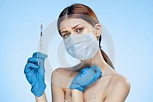 Young beautiful woman in medical mask and rubber gloves holds syringe on blue background, medicine, plastic surgery