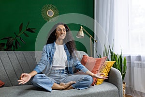 Young beautiful woman meditating in lotus pose, Hispanic woman smiling contentedly dreaming about future plans, sitting