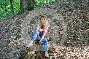 Young beautiful woman model with long hair in jeans and a tank top walks through the forest park among trees and vegetation posing