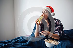 Young beautiful woman in morning bed at home. Christmas time or ney year period. Female model in red hat watching tv or